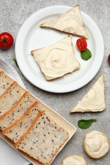 Plates of tasty toasts with cream cheese and fresh bread on grey background