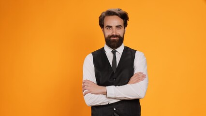 Before serving meal, elegant waiter poses with reliability in front of a yellow background in studio. Bearded server in suit operating in formal environment in the culinary sector. - obrazy, fototapety, plakaty