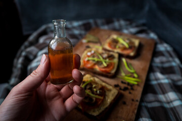 Small bottle of sause in a woman's hand,  sandwiches on a kitchen board with a tablecloth,  rye...