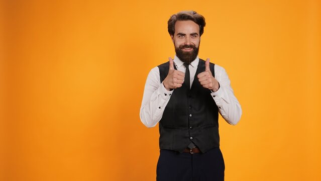 Satisfied waiter does positive gesture while showing his appreciation. Working in the culinary sector, professional staff member gives thumbs up as an excellent statement, like symbol.