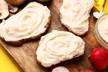 Wooden board of tasty sandwiches with cream cheese on yellow background