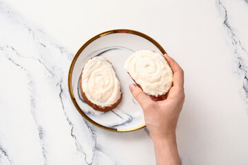 Woman eating tasty sandwiches with cream cheese on white marble background