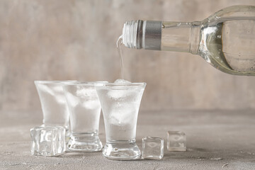 Pouring of vodka from bottle into shot on grey background