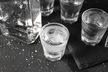 Shots and bottle of vodka with ice cubes on black background
