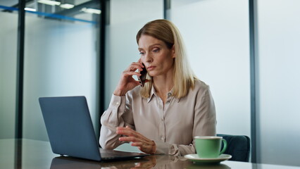 Serious entrepreneur talking mobile phone in office. Woman having cellphone call