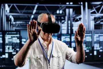 Elderly adept technician immersed in virtual reality at data center, doing infrastructure...