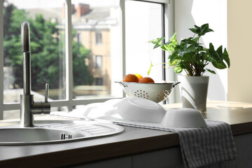 Clean bowls on wooden kitchen counter with sink, houseplant, colander and fruits, closeup