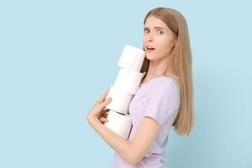 Surprised young woman with stack of toilet paper on color background