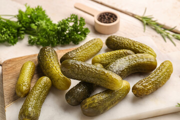 Board with pickled cucumbers and different spices on white wooden background