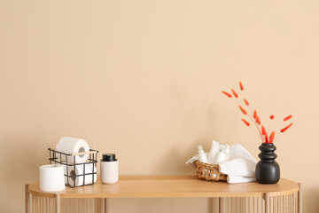 Basket with toilet paper rolls, cosmetic products and dried flowers on wooden table near color wall