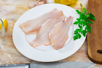 Raw rockfish fillet on plate, garlic, parsley and salt on wooden table. Ingredients for cooking