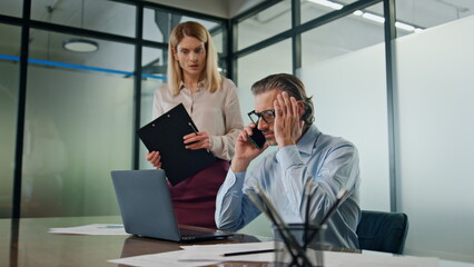 Nervous businessman talking smartphone at office. Stressed couple working laptop