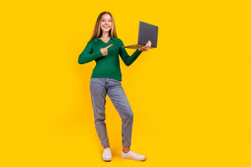 Full length photo of cheerful teenage blonde hair girl recommendation point finger laptop for studying isolated on yellow color background