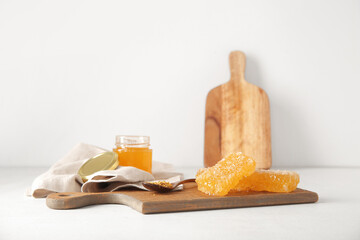 Wooden board with honeycombs and bee pollen on light background