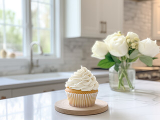 white frosted vanilla cupcake on a counter top in a white kitchen, bright and airy, white roses in...
