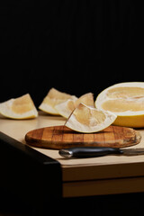 A pomelo fruit on the kitchen table, cut into several pieces, lies on a cutting board, and a...