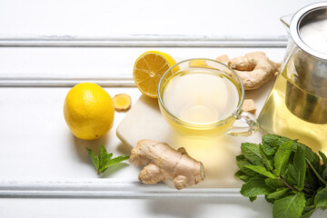 Glass cup of ginger tea with lemon and mint on white background