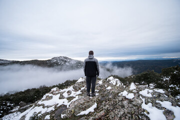 Joven en la cima de una montaña nevada mirando el paisaje con nubes