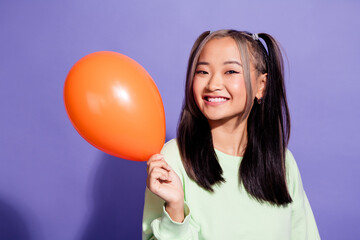 Portrait of cheerful youth japanese girl ponytails in green jumper holding orange air balloon...