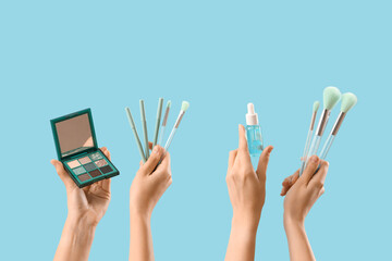 Women with makeup brushes, eyeshadows and serum on blue background