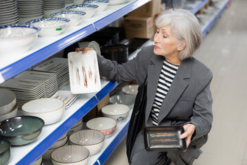 Interested elderly woman choosing square ceramic Asian style plates for serving sushi in tableware...