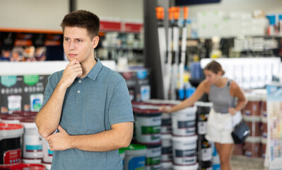 Thoughtful man standing in paint supplies store and planning to paint walls in apartment during...