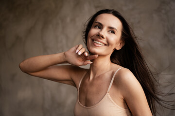 Photo with no filters of lovely lady after shower smiling and applying cream on face isolated on grey concrete wall background