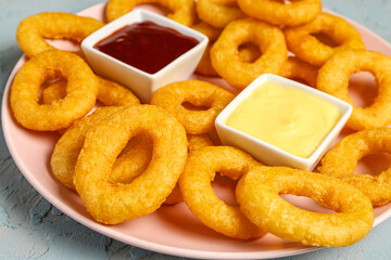 Plate with fried breaded onion rings and different sauces on blue background
