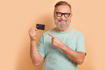 Portrait of toothy beaming senior man in glasses wear stylish t-shirt indicating at debit card...