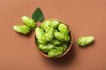 Bowl with fresh green hops on brown background