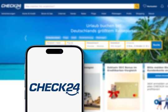Smartphone zeigt Check 24 Logo an, im Hintergrund die Website des Vergleichsportal f&uuml;r Versicherungen, Finanzen, Energie, Telekommunikation, Reisen und Shopping