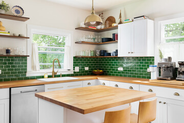 A kitchen detail with butcher block wood countertops, white cabinets, a gold fixture hanging over the island, and green subway tile backsplash. No brands or logos. - obrazy, fototapety, plakaty