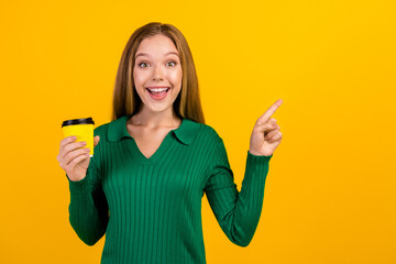 Photo of young excited girl teenager loves this cafeteria pointing finger copyspace holding free coffee isolated on yellow color background