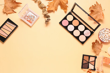 Composition with different eye shadows palettes and autumn leaves on beige background