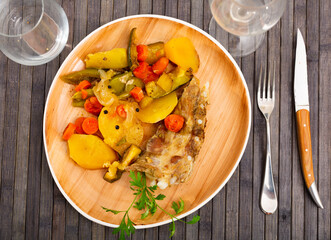 Appetizing baked pork ribs with potatoes and vegetables, decorated with a fresh sprig of parsley