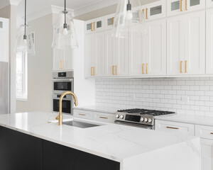 A kitchen detail with white cabinets, a large black island, gold hardware, and black lights hanging...