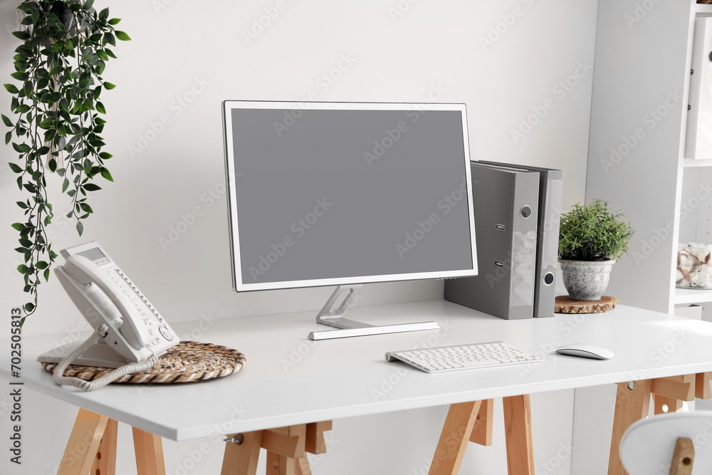 Poster blank computer monitor with telephone on table in light office