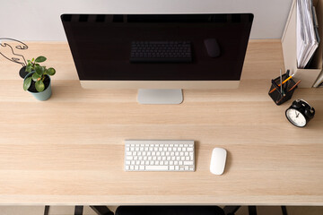Blank computer monitor with alarm clock on table in office, top view