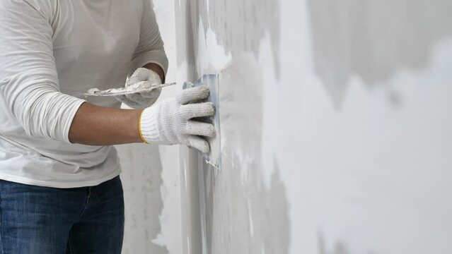 Plasterwork and wall painting preparation. Asian male applying filling drywall patch.