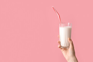 Hand holding glass of milk with straw on pink background - obrazy, fototapety, plakaty
