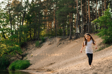 Happy little girl running on sandy beach close to river. Junior active athlete doing sports and...