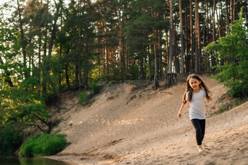 Happy little girl running on sandy beach close to river. Junior active athlete doing sports and having fun near water.