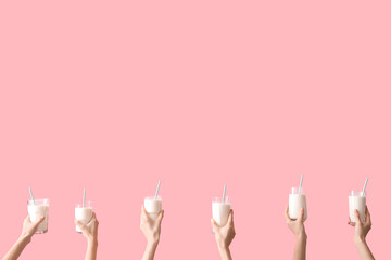 Hands with glasses of milk on pink background