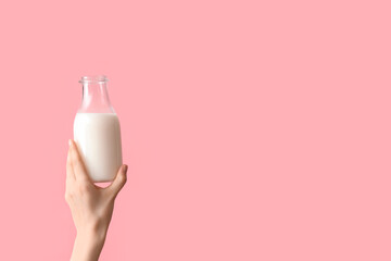 Hand holding bottle of milk on pink background