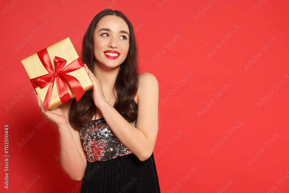 Poster Beautiful young woman with Christmas gift on red background, space for text