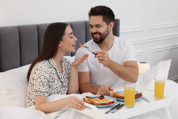 Happy couple having breakfast on bed at home