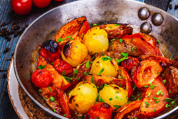 Roasted cherry tomatoes in cast iron skillet on wooden table.