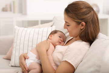 Mother holding her cute newborn baby on sofa indoors, space for text - obrazy, fototapety, plakaty