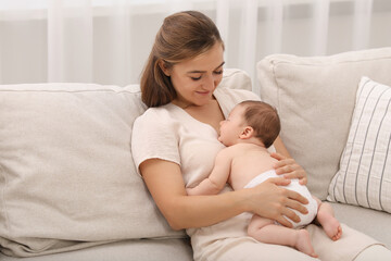 Obraz na płótnie Canvas Mother holding her cute newborn baby on sofa indoors
