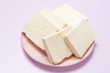 A sliced pieces of tofu on a pink plate on lilac background close-up, side view.